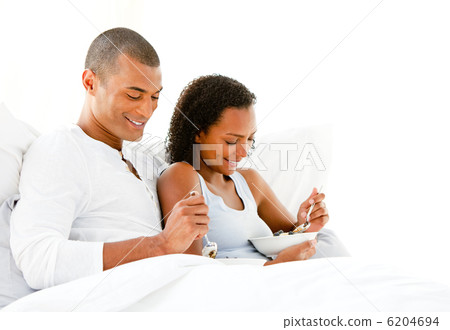 Smiling couple having breakfast lying on their bed Smiling couple having breakfast lying on their bed 6204694
