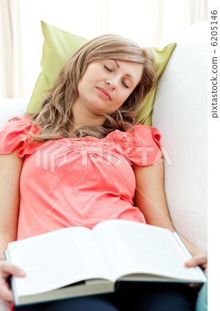 Tired woman reading a book lying on a sofa in the living-room 6205146