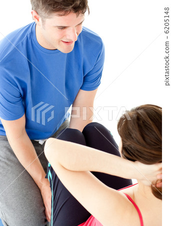 Brunette woman doing sit-ups assited by her personal trainer 6205148
