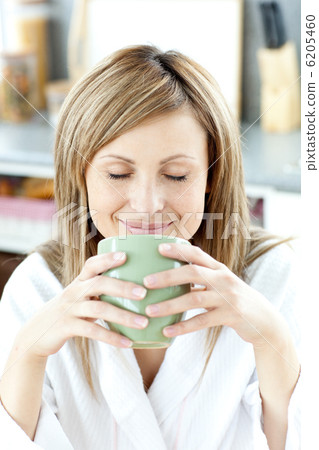Delighted woman holding a cup a tea in the kitchen Delighted woman holding a cup a tea in the kitchen 6205460