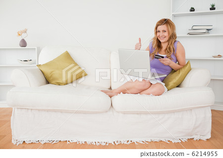 Happy woman sitting on a sofa is going to make a payment on the Happy woman sitting on a sofa is going to make a payment on the 6214955
