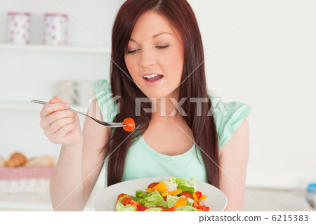 Charming red-haired woman enjoying a mixed salad in the kitchen 6215383