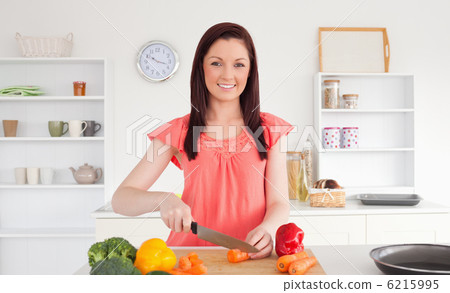 Beautiful red-haired woman cutting some vegetables in the kitche 6215995