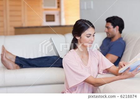 Woman reading a book while her fiance is using a laptop Woman reading a book while her fiance is using a laptop 6218874