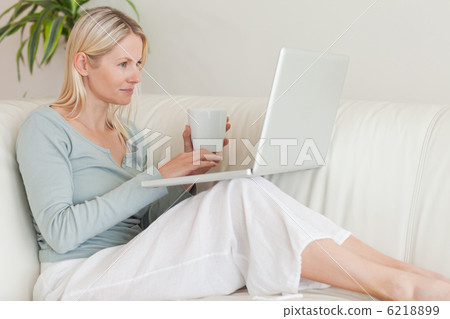 Woman sitting on the couch with a cup of coffee and her laptop Woman sitting on the couch with a cup of coffee and her laptop 6218899