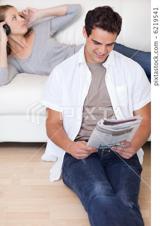 Man reading the news while his girlfriend is listening to music 6219541