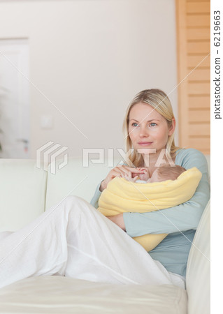Mother sitting on the couch while holding her baby 6219663