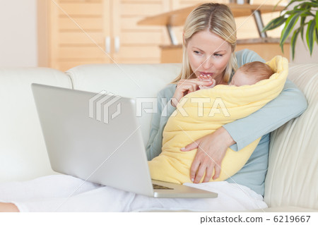 Mother holding her baby while looking at her laptop Mother holding her baby while looking at her laptop 6219667
