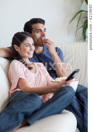 Portrait of a couple watching TV while eating popcorn Portrait of a couple watching TV while eating popcorn 6219697