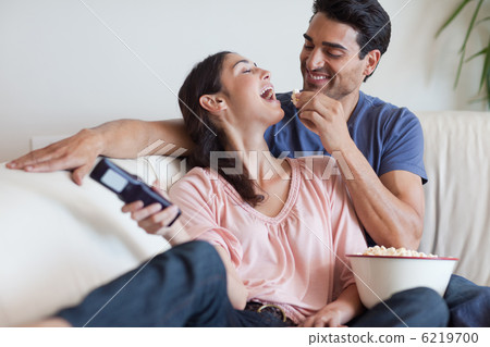 Playful couple watching TV while eating popcorn Playful couple watching TV while eating popcorn 6219700