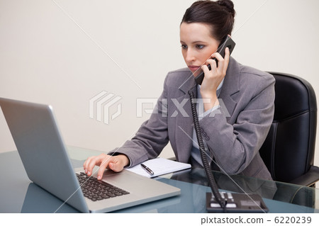 Businesswoman typing on her laptop while on the telephone Businesswoman typing on her laptop while on the telephone 6220239