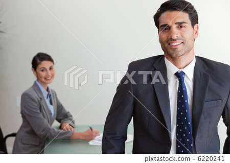 Good looking businessman posing while his colleague is working 6220241