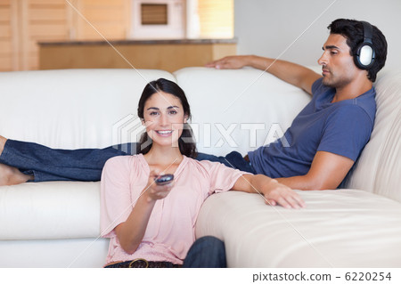 Woman watching television while her husband is listening to musi Woman watching television while her husband is listening to musi 6220254