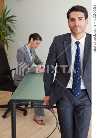 Portrait of a businessman posing while his colleague is working Portrait of a businessman posing while his colleague is working 6220582