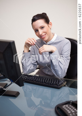 Smiling businesswoman with pen sitting at her desk Smiling businesswoman with pen sitting at her desk 6220837