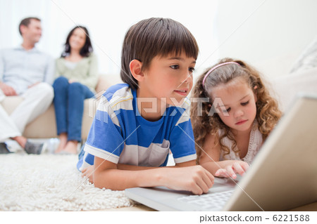 Kids using laptop on the carpet with parents behind them 6221588