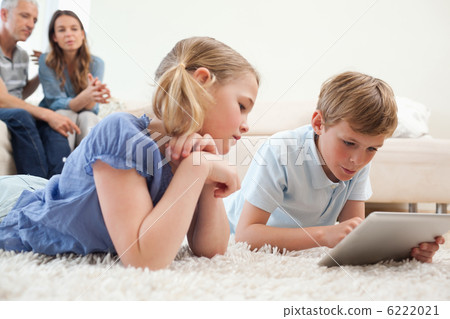 Siblings using a tablet computer with their parents on the backg 6222021