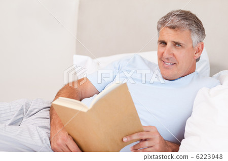 Smiling man with book in bed Smiling man with book in bed 6223948