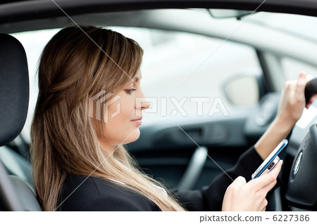 Beautiful businesswoman sending a text while driving 6227386