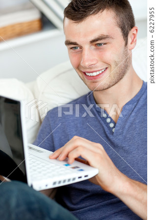 Joyful young man sitting on the sofa using his laptop Joyful young man sitting on the sofa using his laptop 6227955