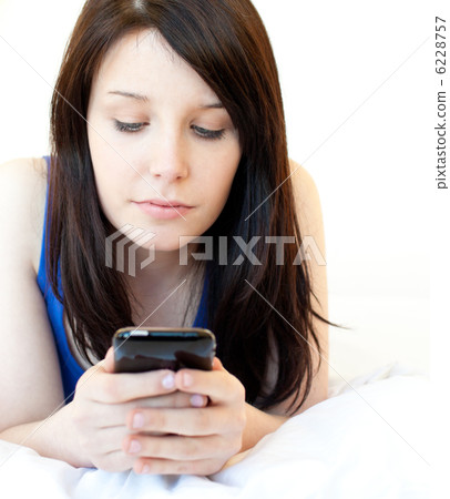Concentrated young woman texting while lying on a bed Concentrated young woman texting while lying on a bed 6228757