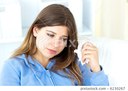 Sad young woman holding tissues sitting in the living-room Sad young woman holding tissues sitting in the living-room 6230267