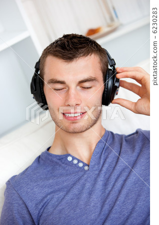Relaxed young man listening to music with headphones in the livi Relaxed young man listening to music with headphones in the livi 6230283