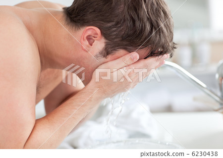 Cute caucasian man spraying water on his face after shaving in t Cute caucasian man spraying water on his face after shaving in t 6230438