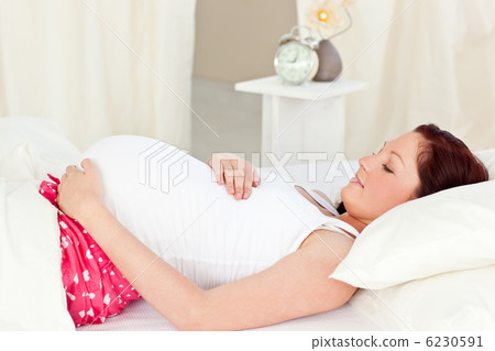 Portrait of a happy pregnant woman lying on bed and touching her Portrait of a happy pregnant woman lying on bed and touching her 6230591
