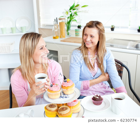 Female friends with cakes and coffee speaking together in the ki Female friends with cakes and coffee speaking together in the ki 6230774