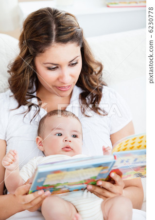 Attentive mother reading a book to her adorable baby sitting in Attentive mother reading a book to her adorable baby sitting in 6230778