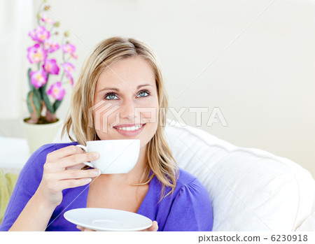 Bright woman enjoying her coffee sitting on a sofa in the living Bright woman enjoying her coffee sitting on a sofa in the living 6230918