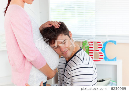 careful young man listening to the belly of his pregnant wife in careful young man listening to the belly of his pregnant wife in 6230969