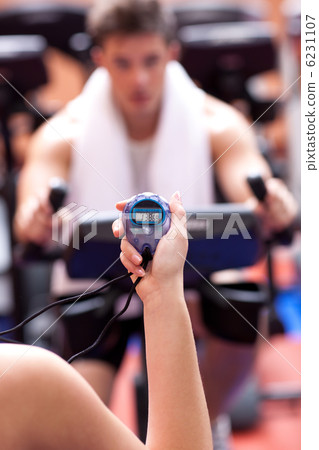 Caucasian woman holding a chronometer and man doing physical exe 6231107