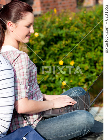 Charming female student using a laptop and sitting behind her bo Charming female student using a laptop and sitting behind her bo 6231652