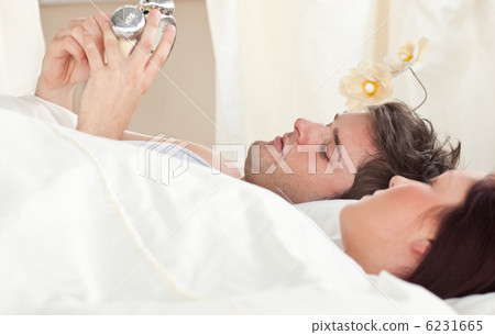 Young caucasian couple holding an alarm clock in bed before slee 6231665