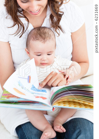 Happy mother showing a book to her baby sitting in the sofa at h 6231669
