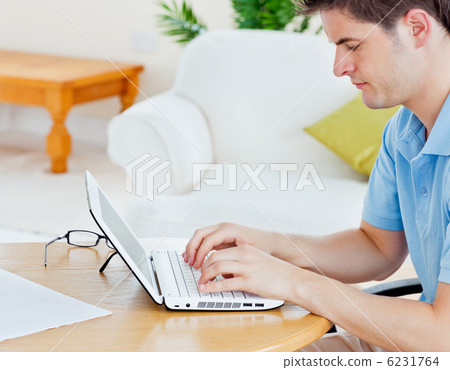 focused handsome man working on his laptop sitting in the living focused handsome man working on his laptop sitting in the living 6231764