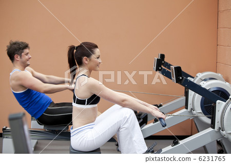 Young couple using a rower in a sport centre Young couple using a rower in a sport centre 6231765