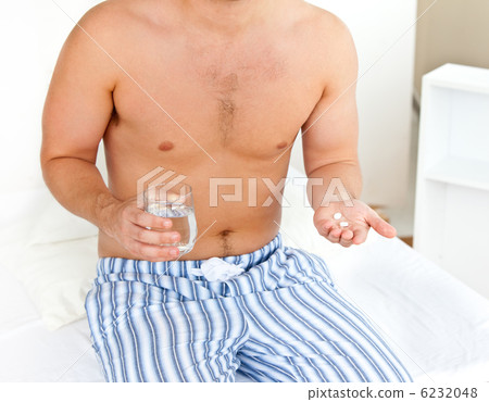 Depressed young man sitting on his bed and holding a glass of wa Depressed young man sitting on his bed and holding a glass of wa 6232048