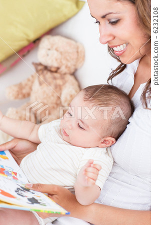 Portrait of joyful mother reading a book to her baby sitting in Portrait of joyful mother reading a book to her baby sitting in 6232108