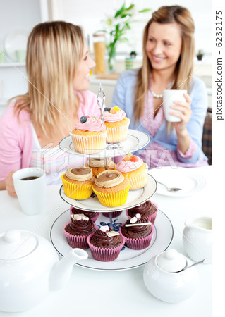 Two cute friends eating cupcakes sitting in the kitchen at home Two cute friends eating cupcakes sitting in the kitchen at home 6232175