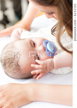 Close-up of a baby lying on a changing table while his mother is 6232181