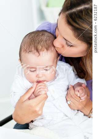 Portrait of an adorable mother kissing her baby iin the kitchen Portrait of an adorable mother kissing her baby iin the kitchen 6232187