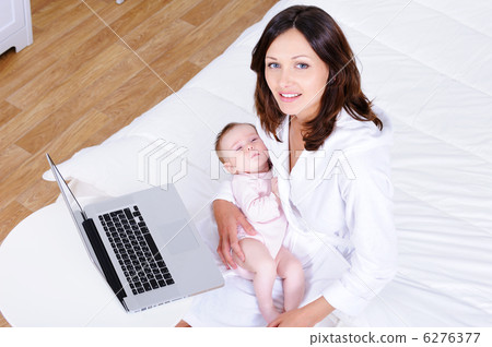 Woman with baby sitting on a bed with laptop - high angle Woman with baby sitting on a bed with laptop - high angle 6276377