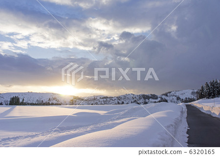Sinking sun and snowy landscape and a lonely road Uonuma City 6320165