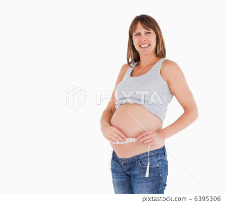 Pretty pregnant woman measuring her belly while standing Pretty pregnant woman measuring her belly while standing 6395306