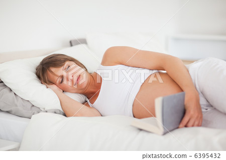 Beautiful pregnant woman reading a book while lying on her bed Beautiful pregnant woman reading a book while lying on her bed 6395432