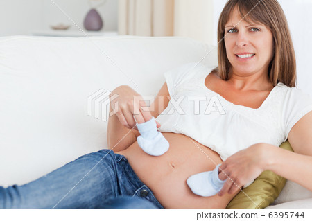 Young pregnant woman playing with baby shoes while lying 6395744
