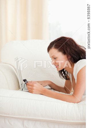 Joyful woman working on notebook with credit card in hand 6398867
